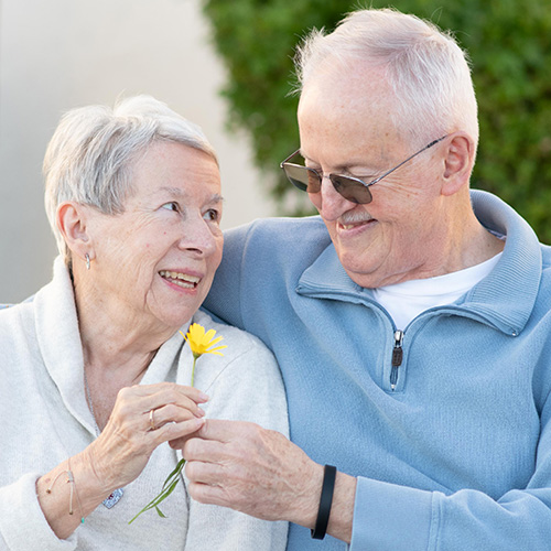Husband and wife sitting on a bench. Husband giving wife a flower.